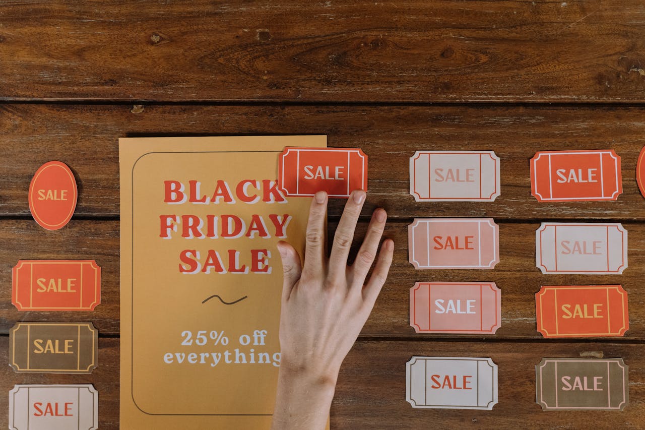 Top view of hand arranging Black Friday sale flyers on wooden table, offering 25% off everything.